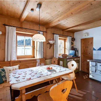 Ein gemütlicher Essbereich in einem Holzhaus mit einem langen Tisch und Stühlen. Die Wände sind aus Holz, und große Fenster lassen viel Licht herein.