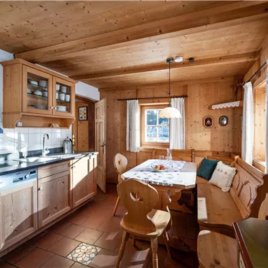 Eine gemütliche Küche mit Holzoberflächen und einem Essbereich. Das Licht fällt durch ein Fenster und schafft eine einladende Atmosphäre.