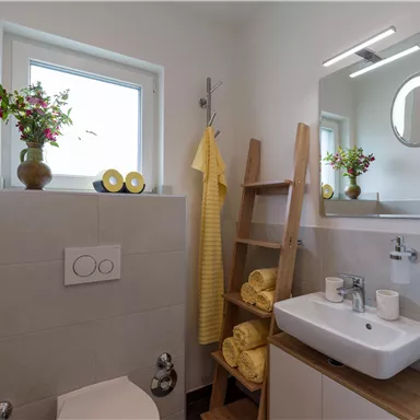 A modern bathroom with a bright design and elegant furnishings. Yellow towels and plants provide a friendly accent.