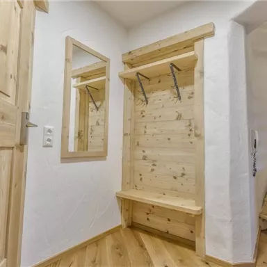 Ein heller Eingangsbereich mit Holzpaneelen und einem großen Spiegel. An der Wand befinden sich Kleiderhaken und eine Sitzgelegenheit.