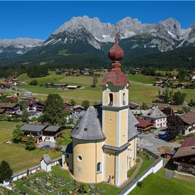 A picturesque church with a golden dome stands in the center of a charming village. In the background, impressive mountains and green meadows are visible.