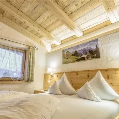 Ein gemütliches Schlafzimmer mit Holzdecke und sanfter Beleuchtung. Es gibt ein großes Bett mit Kissen und ein Fenster mit Blick auf die Berge.