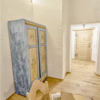 Eine helle und gemütliche Innenansicht mit einem blauen Schrank und einem Holztisch. Die Wände sind hell und der Boden ist aus Holz, was eine warme Atmosphäre schafft.