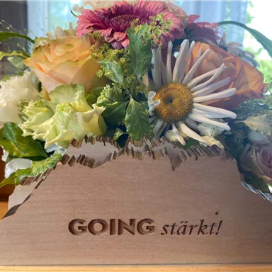 A beautiful bouquet of colorful flowers and green leaves in a wooden box. The box has the inscription "GOING strengthens!".
