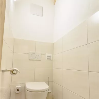 Ein modernes Badezimmer mit einer weißen Toilette und hellem Fliesenboden. Die Wände sind in neutralen Farben gehalten und eine Holzdecke sorgt für ein warmes Ambiente.