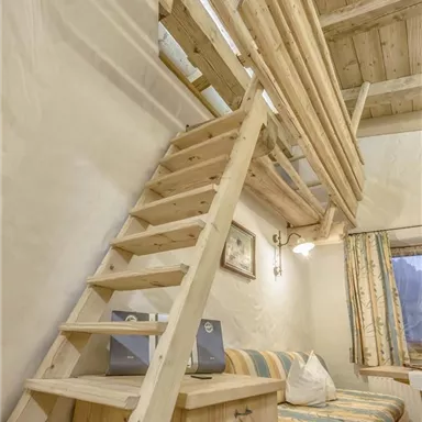 Ein gemütlicher Raum mit Holzdecke und einer Treppe zu einem Schlafbereich oben. Die Einrichtung ist einfach und einladend, ideal zum Entspannen.