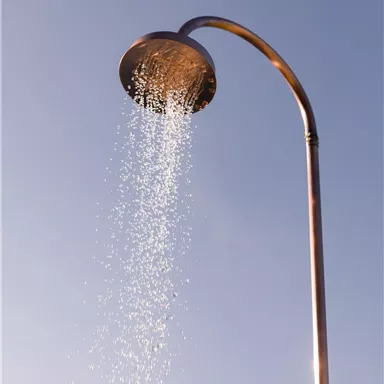 A shower facility with bubbling water under a clear sky. The metal structure is modern and simply designed.