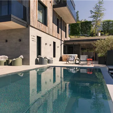 Ein modernes Haus mit einer stilvollen Terrasse und einem Pool. Die Umgebung ist grün und einladend.