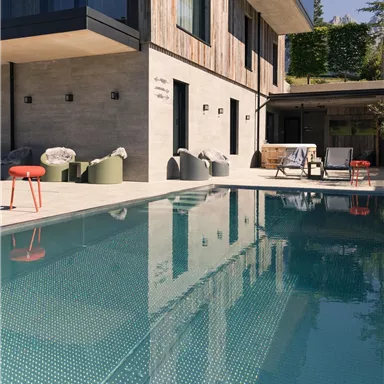 Ein modernes Haus mit einem Pool und schöner Terrasse. Die klare Wasseroberfläche spiegelt die Architektur des Gebäudes wider.
