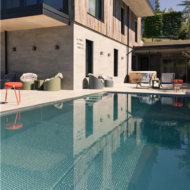 A modern house with a wooden facade and a clear swimming pool. The terrace is furnished with cozy furniture.