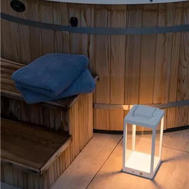 Ein gemütlicher Wellnessbereich mit einem Whirlpool, einem Handtuch und einer beleuchteten Laterne. Die Holzverkleidung und der geflieste Boden schaffen eine entspannende Atmosphäre.