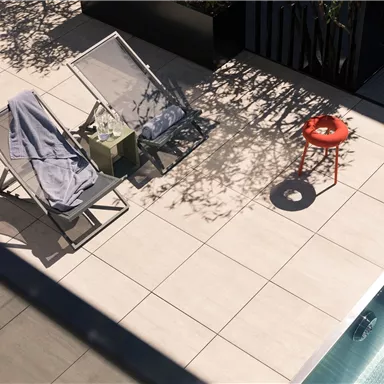 A sunny pool area with loungers and a red stool. Cool shadows fall on the tiles.