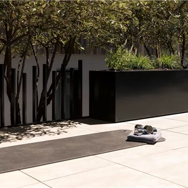 A beautiful outdoor area with a yoga mat on the floor. The surroundings are filled with plants and modern elements.