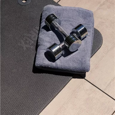 A towel is lying on a training mat, and a dumbbell is on top of it. The surface is bright and modernly designed.
