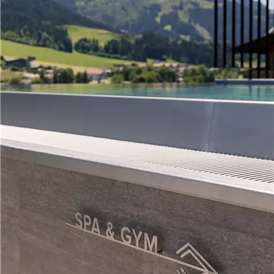 A part of a wellness area with a sign for "SPA & GYM". In the background, green hills and a clear, sunny sky are visible.