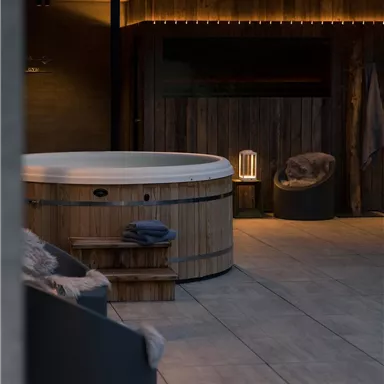 A modern spa with a wooden hot tub and comfortable seating. Soft lighting creates a relaxed atmosphere.