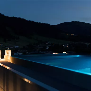Ein luxuriöser Infinity-Pool in der Abenddämmerung. Sanfte Lichter und die umliegenden Berge schaffen eine entspannende Atmosphäre.