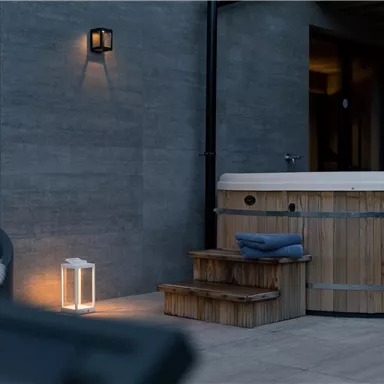 A modern wooden hot tub is situated on a terrace with gray walls. Next to the hot tub are stairs and a stylish lantern.
