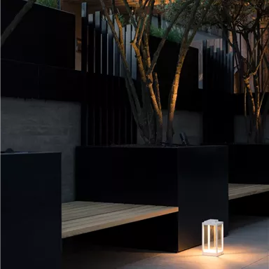 A modern seating option made of black wood and concrete. A soft light shines from a lantern in the dusk.