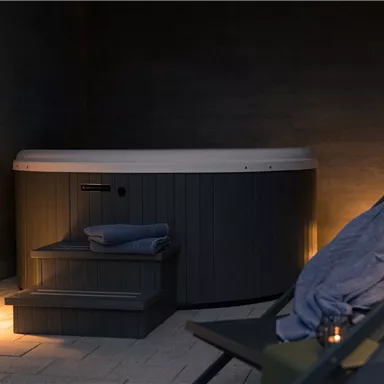 A modern whirlpool in a cozy indoor setting. Next to the whirlpool, there is a comfortable lounger and stylish lighting.