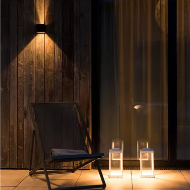A cozy chair is positioned in front of a glass sliding door. Soft light illuminates the surroundings, and two lanterns create an inviting atmosphere.