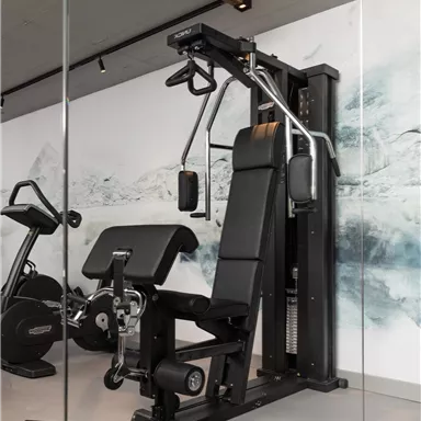 Ein modernes Fitnessstudio mit einer Kraftmaschine und einer Hantelbank. Im Hintergrund ist eine stylische Wandgestaltung zu sehen.