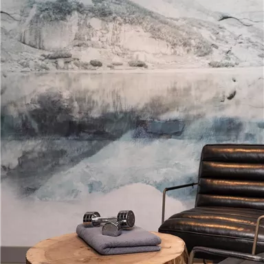 Ein modernes Wohnzimmer mit einem runden Holztisch und einem schwarzen Sessel. Die Wand ist mit einem malerischen Landschaftsbild dekoriert.