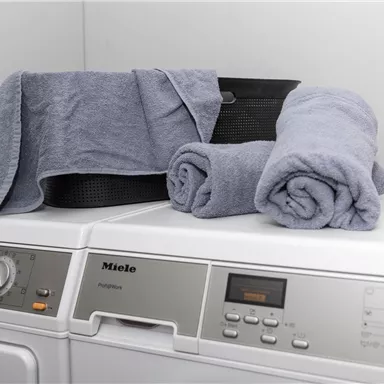 Ein Miele-Waschgerät mit frischen, grauen Handtüchern und einem schwarzen Korb. Die Handtücher sind ordentlich auf den Geräten drapiert.