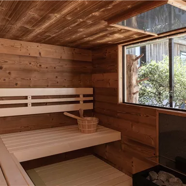 Eine gemütliche Sauna mit Holzvertäfelungen und Bankreihen. Durch das Fenster ist die schöne Landschaft sichtbar.