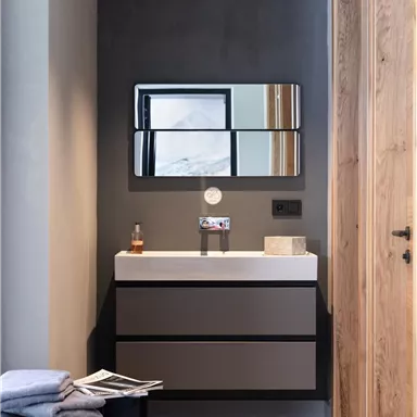 A modern bathroom with an elegant sink and a large mirror. The walls are simple, and wooden details create a cozy atmosphere.