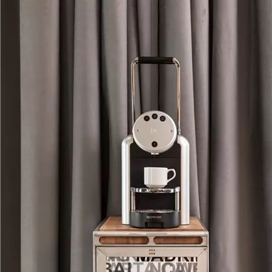 Eine elegante Kaffeemaschine steht auf einem Tisch. Der Hintergrund besteht aus grauen Vorhängen.