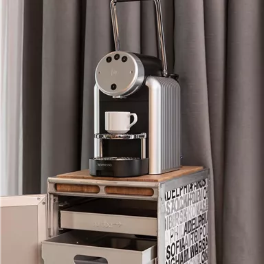 A modern coffee machine is on a table with drawers. Next to the machine stands a white cup, ready for fresh coffee.