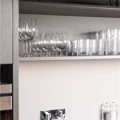 A modern kitchen cabinet with various glasses. The surface is made of gray stone, and there is a water pipe underneath.