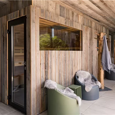 Ein moderner Wellnessbereich mit Holzverkleidung und großen Fenstern. Bequeme Sitzgelegenheiten und eine entspannende Atmosphäre laden zum Verweilen ein.