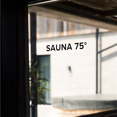 A window with the inscription "SAUNA 75°". In the background, a modern, bright room can be seen.