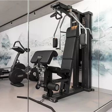Ein modernes Fitnessstudio mit verschiedenen Trainingsgeräten. Im Vordergrund steht eine multifunktionale Kraftstation.