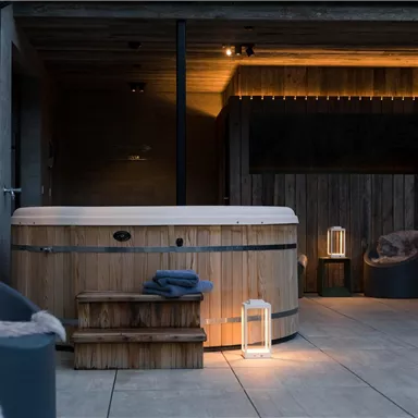 Ein gemütlicher Außenbereich mit einem Holz-Whirlpool. Sanfte Beleuchtung und Dekoration schaffen eine entspannte Atmosphäre.