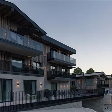 Ein modernes Gebäude mit mehreren Balkonen und großen Fenstern. Die Architektur kombiniert Holz und Glas und bietet eine elegante Optik.