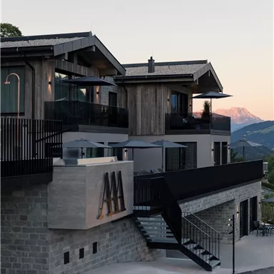 Ein modernes Gebäude mit Holz- und Steinelementen, umgeben von Berglandschaft. Die Fassade ist stilvoll und einladend, ideal für einen entspannten Aufenthalt.