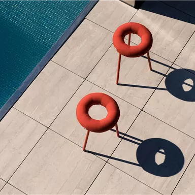 Two modern, red-orange chairs are standing next to a pool. The chairs cast interesting shadows on the light ground.