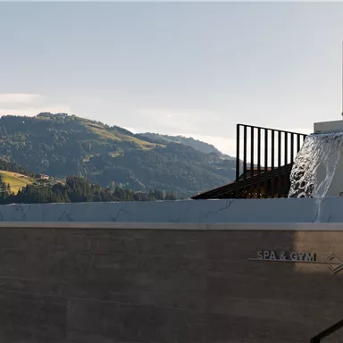 A modern spa area with a waterfall and a view of the green mountains. The place radiates tranquility and relaxation.