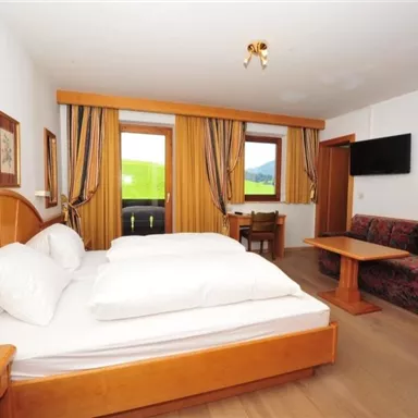 A cozy hotel room with a large bed and a sofa bed. Large windows provide a view of the natural surroundings.