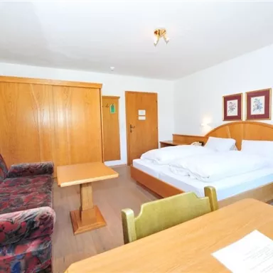A cozy hotel room with a double bed and a couch. There is a table and wooden paneling that creates a warm atmosphere.