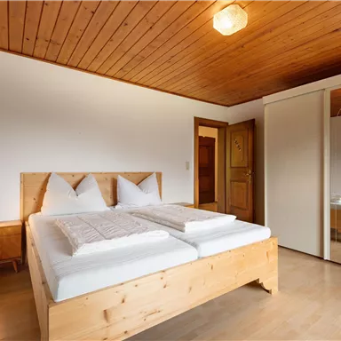 Ein gemütliches Schlafzimmer mit einem Doppelbett aus Holz und zwei Kissen. Der Raum hat warmes Holzdekor und einen großen Spiegel.