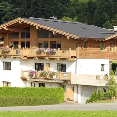 Ein schönes Chalet mit Holzelementen und Blumenkästen. Umgeben von einer grünen Landschaft und Bäumen.