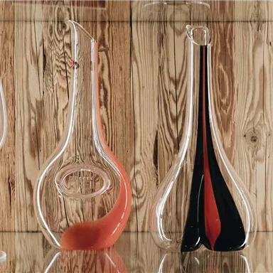 Eine elegante Vitrine mit dekorativen Karaffen und Weingläsern. Die Karaffen sind in verschiedenen Formen und Farben gestaltet.