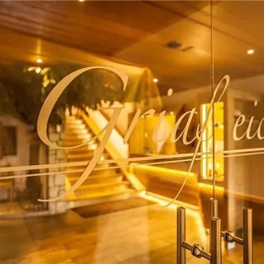 Ein einladender Eingangsbereich mit einer Glastür und warmem Licht. Im Hintergrund sind Treppen und eine gemütliche Atmosphäre zu sehen.