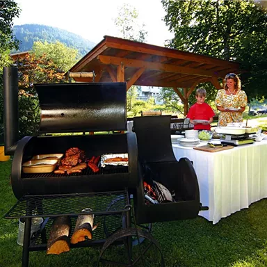 Eine gemütliche Grillparty im Freien mit einem Grill, auf dem verschiedene Fleischsorten zubereitet werden. Im Hintergrund sind zwei Personen, die das Essen vorbereiten, umgeben von viel Grün.