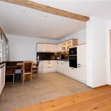 Eine moderne Küche mit hellen Möbeln und Holzdetails. Sie verfügt über einen Esstisch und eine gut ausgestattete Kochzeile.