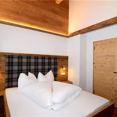 Ein gemütliches Schlafzimmer mit einem großen Bett und Holzvertäfelung. Die Wände sind hell und die Fenster sind mit grünen Vorhängen versehen.